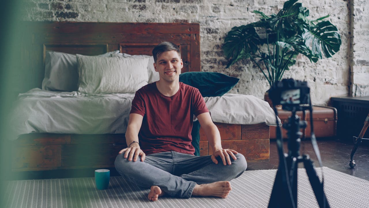 why-choose-us Young adult male vlogger sitting in bedroom, recording content.