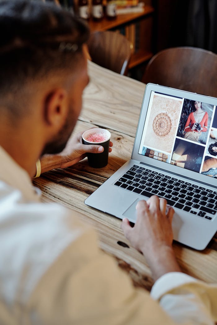services-01 Man focused on work on laptop with artistic images and coffee in a cozy setting.