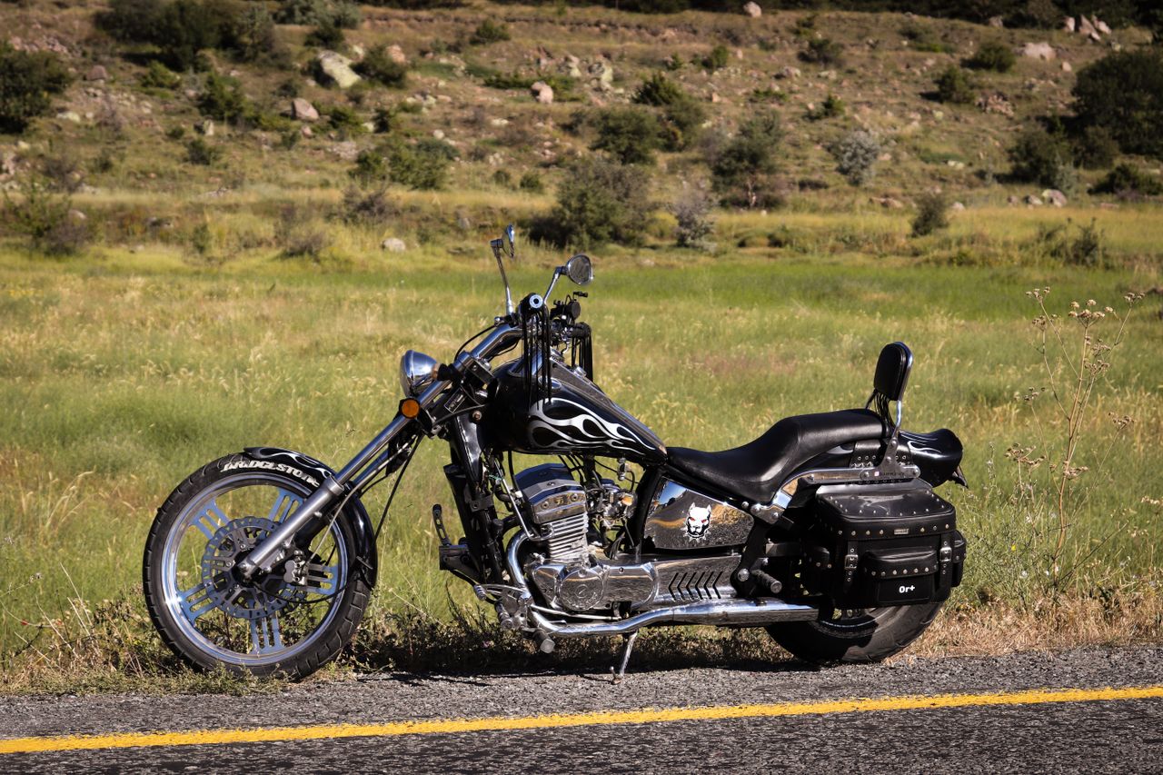 A vintage chopper-style motorcycle with flame design parked on a rural road.