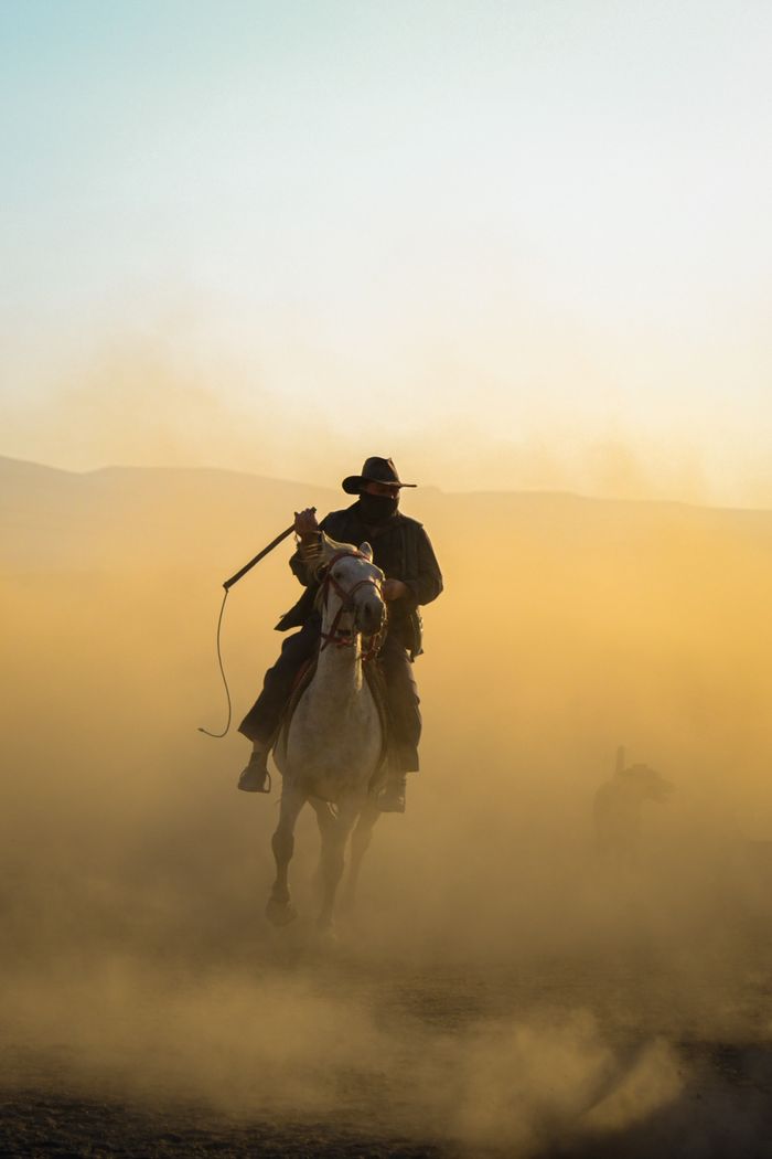 about-us-02 A lone cowboy on horseback navigates a dusty prairie landscape, evoking a sense of adventure.