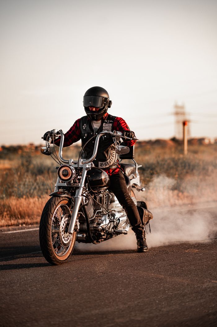 services-01 A motorcyclist in full gear performs a burnout on an open highway at dusk, surrounded by open fields.